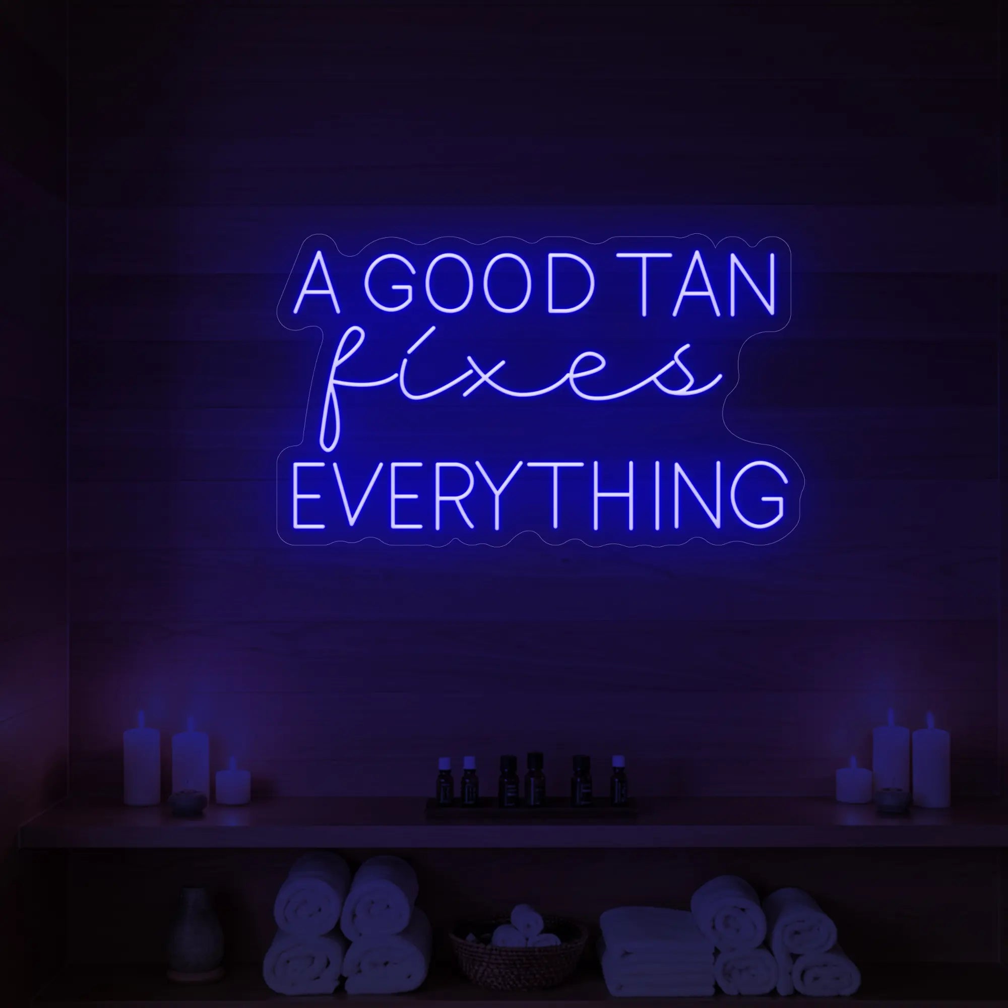 Photo of the 'A GOOD TAN fixes EVERYTHING' neon sign glowing in deep blue against a styled interior wall.