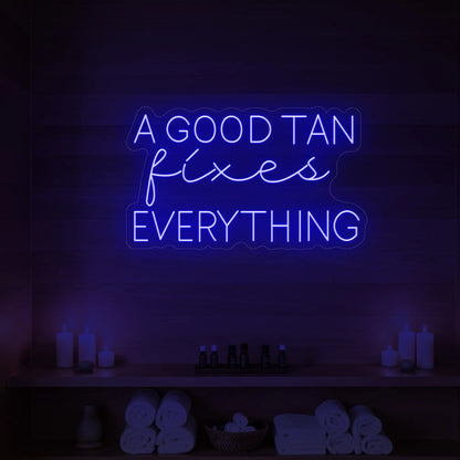 Photo of the 'A GOOD TAN fixes EVERYTHING' neon sign glowing in deep blue against a styled interior wall.