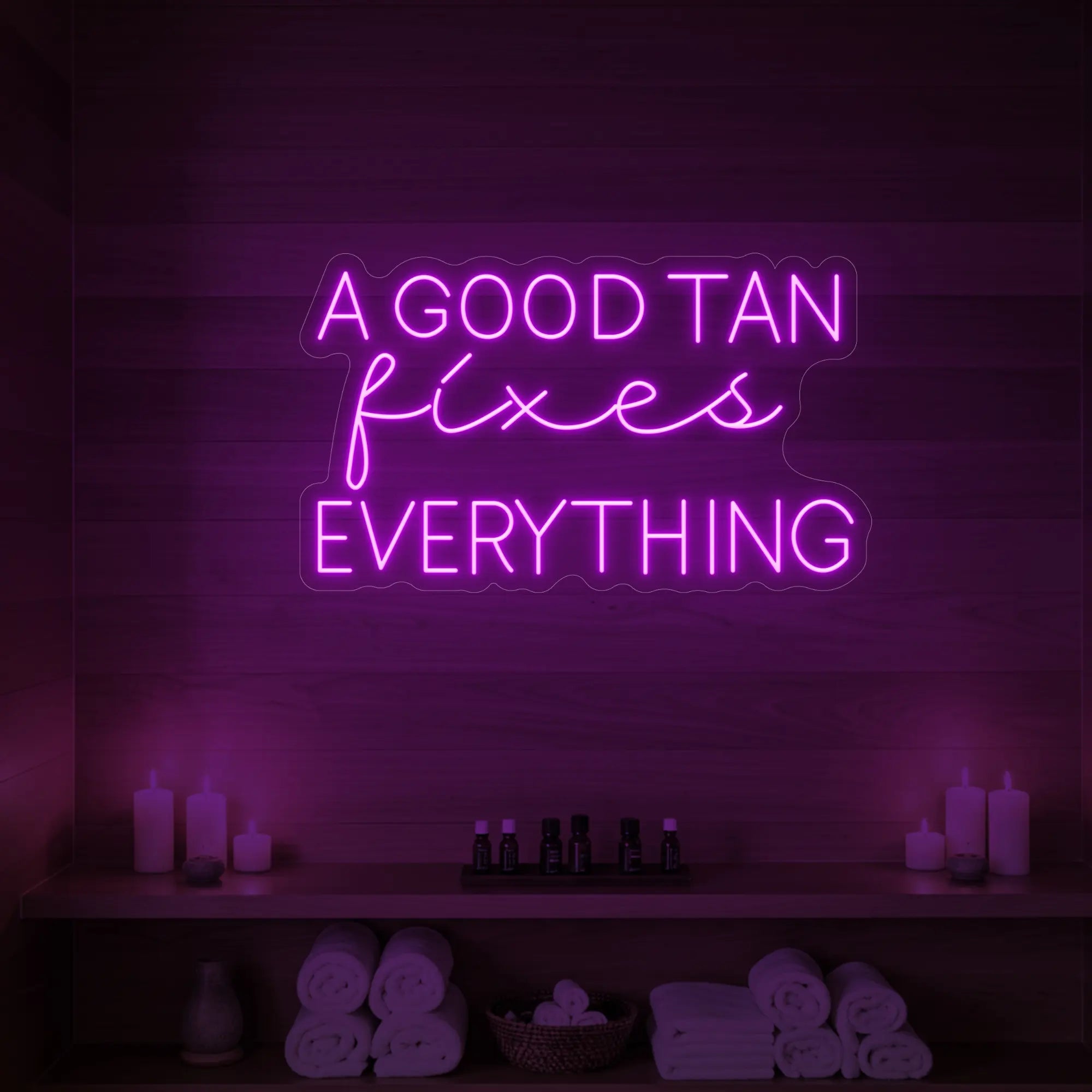 Photo of the 'A GOOD TAN fixes EVERYTHING' neon sign glowing in dark pink against a styled interior wall.