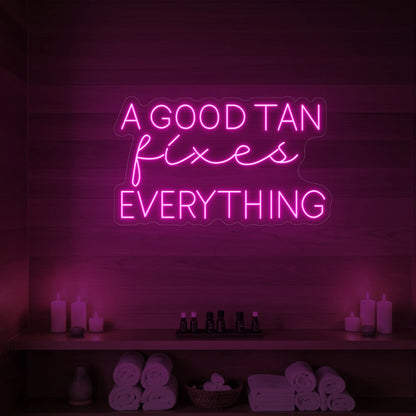 Photo of the 'A GOOD TAN fixes EVERYTHING' neon sign glowing in light pink against a styled interior wall.