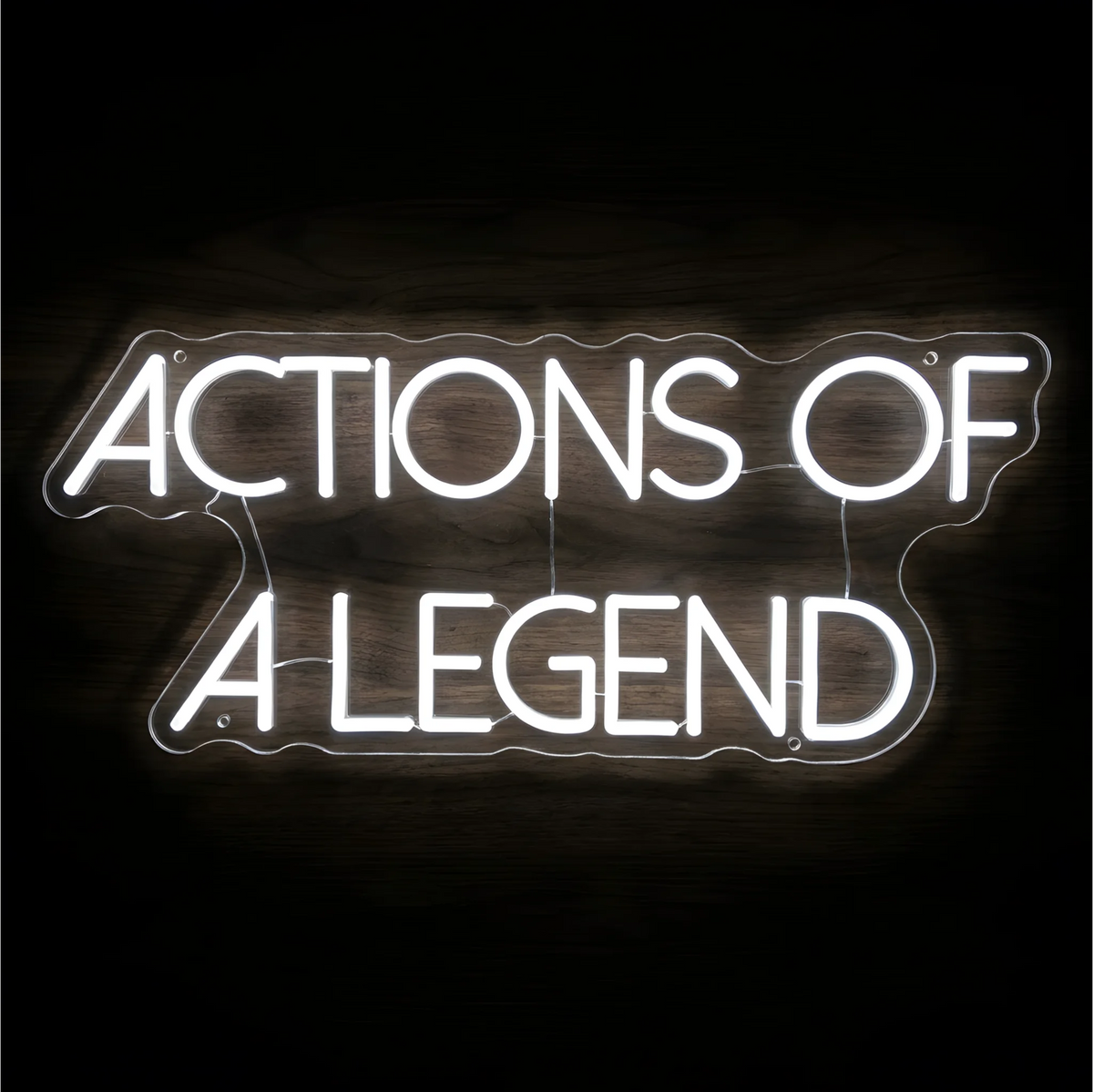 “ACTIONS OF A LEGEND” LED Neon Sign glowing in bright white uppercase letters across two lines on clear acrylic against a dark wood background, suited to home offices and creative workspaces.