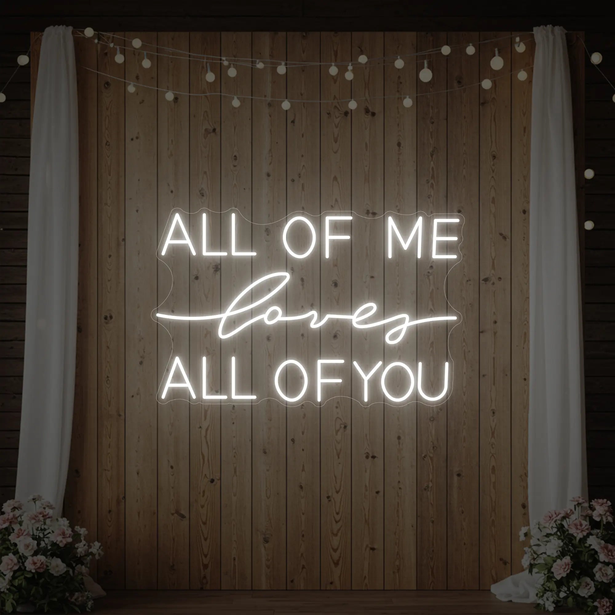 Photo of the 'All Of Me Love All Of You' neon sign glowing in cool white against a styled interior wall.