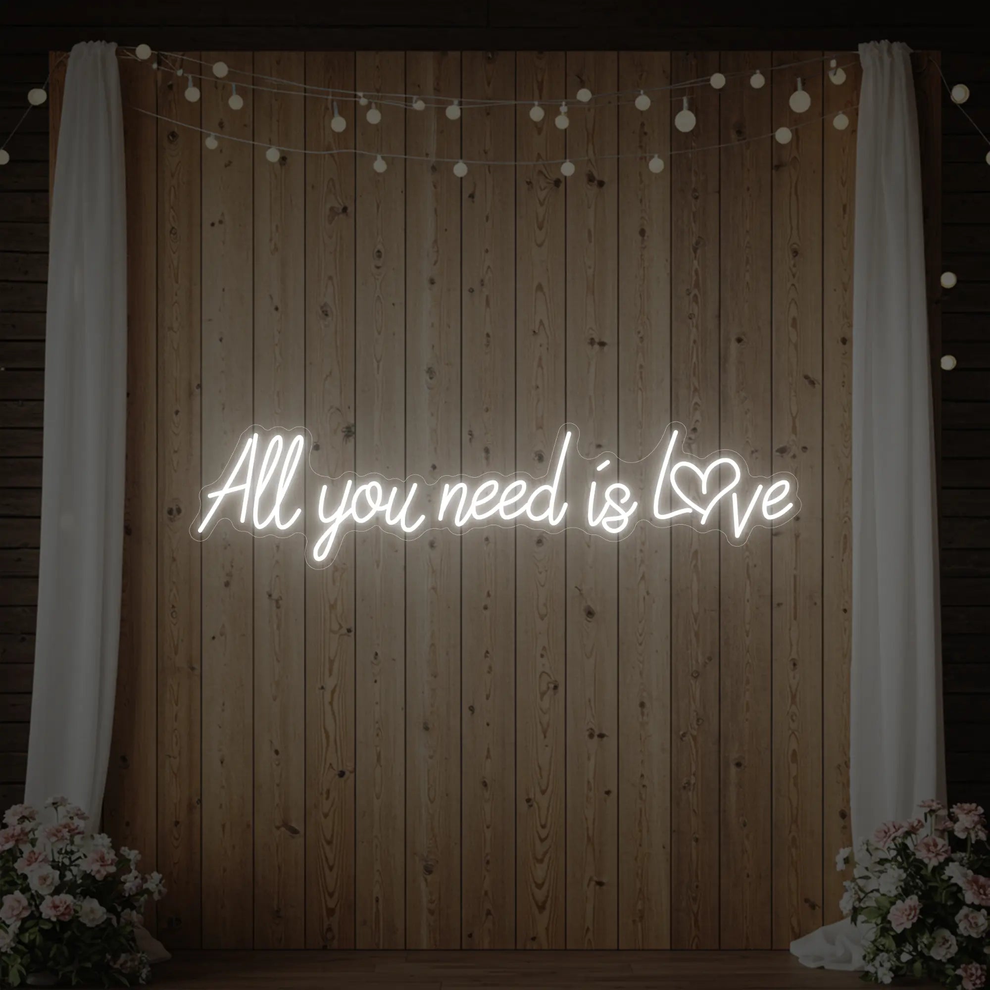 Photo of the 'All You Need Is Love Heart' neon sign glowing in cool white against a styled interior wall.