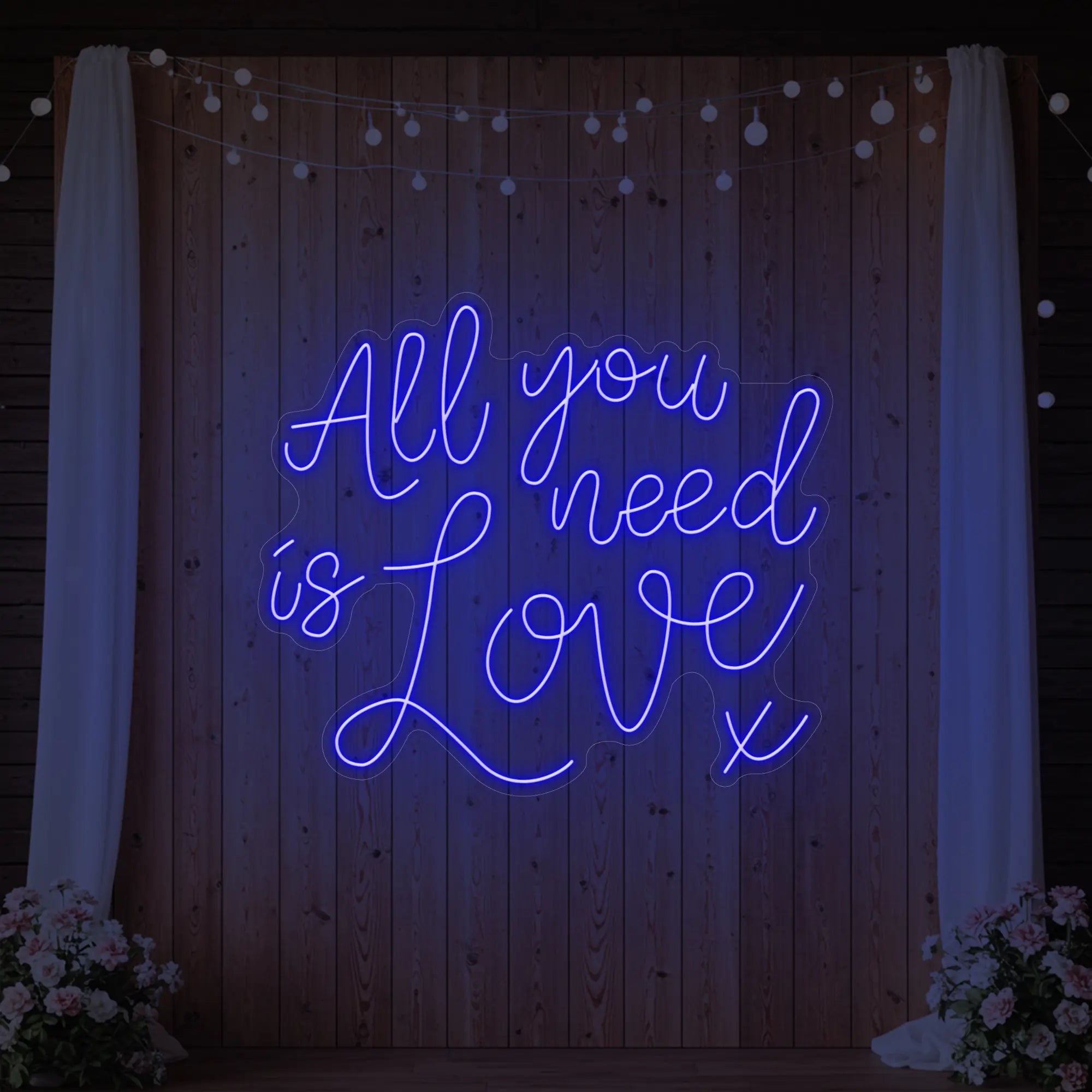 Photo of the 'All You Need Is Love V1' neon sign glowing in deep blue against a styled interior wall.