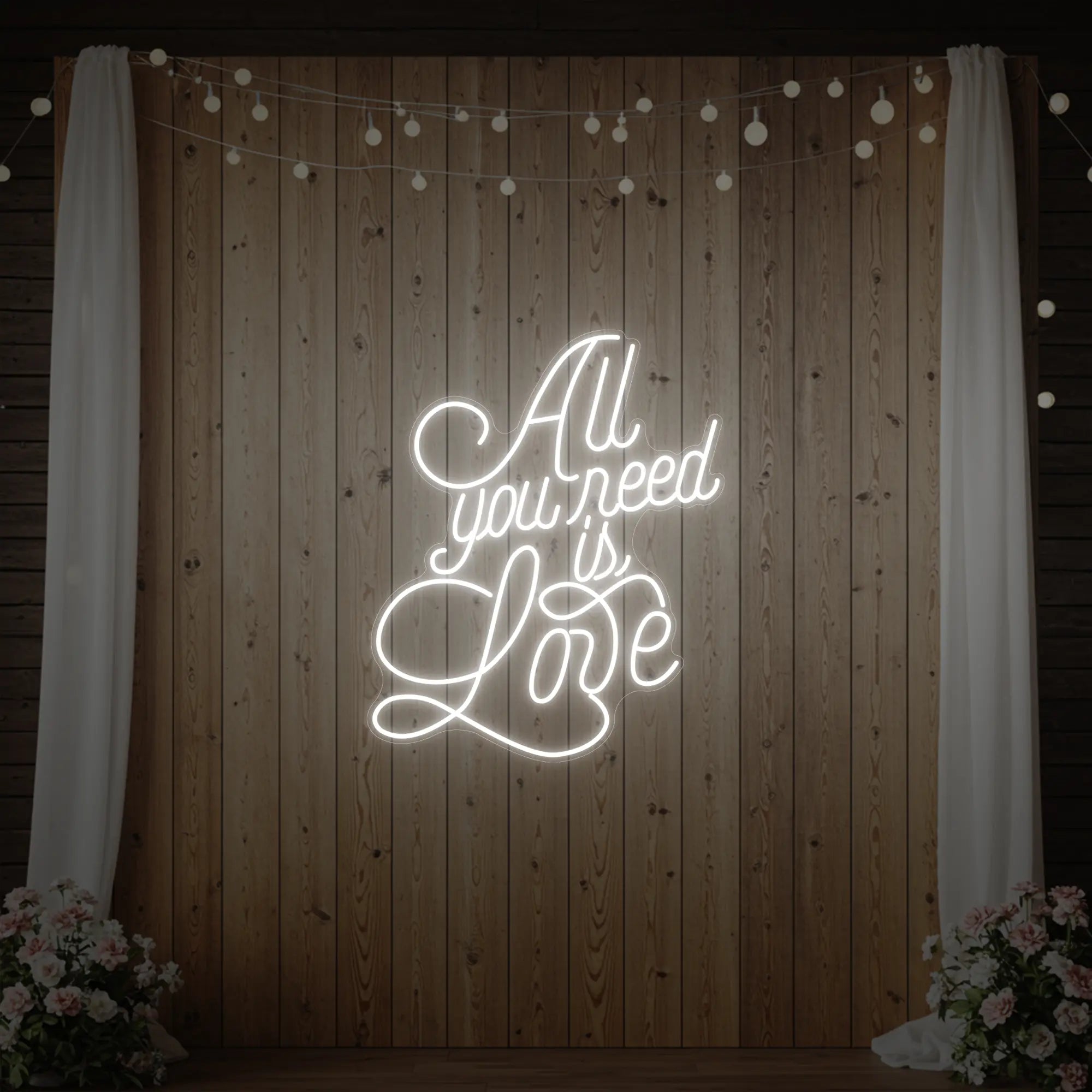 Photo of the 'All You Need Is Love V2' neon sign glowing in cool white against a styled interior wall.