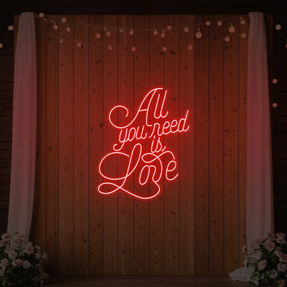Photo of the 'All You Need Is Love V2' neon sign glowing in red against a styled interior wall.