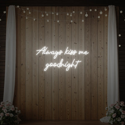 Photo of the 'Always Kiss Me Goodnight' neon sign glowing in cool white against a styled interior wall.