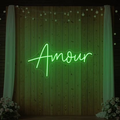 Photo of the 'Amour' neon sign glowing in green against a styled interior wall.