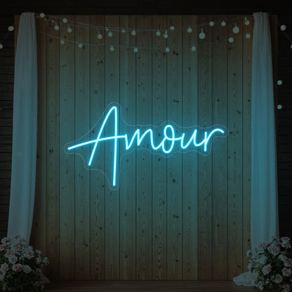 Photo of the 'Amour' neon sign glowing in ice blue against a styled interior wall.