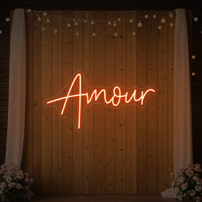 Photo of the 'Amour' neon sign glowing in golden yellow against a styled interior wall.
