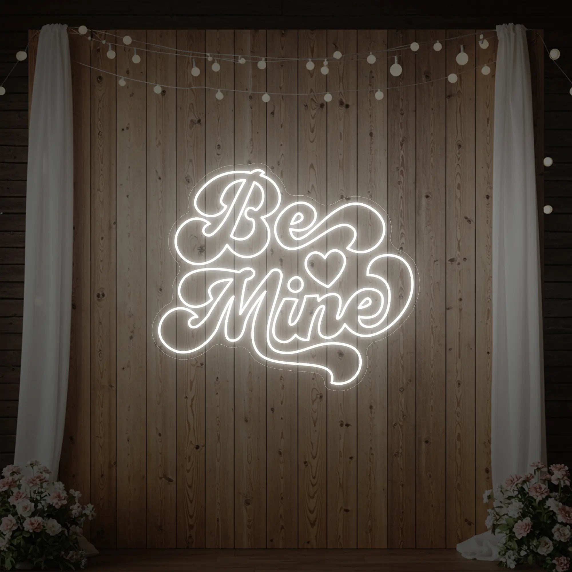 Photo of the 'Be Mine' neon sign glowing in cool white against a styled interior wall.