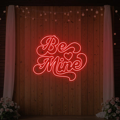 Photo of the 'Be Mine' neon sign glowing in red against a styled interior wall.