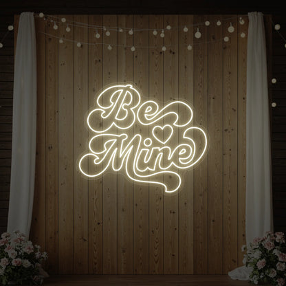 Photo of the 'Be Mine' neon sign glowing in warm white against a styled interior wall.