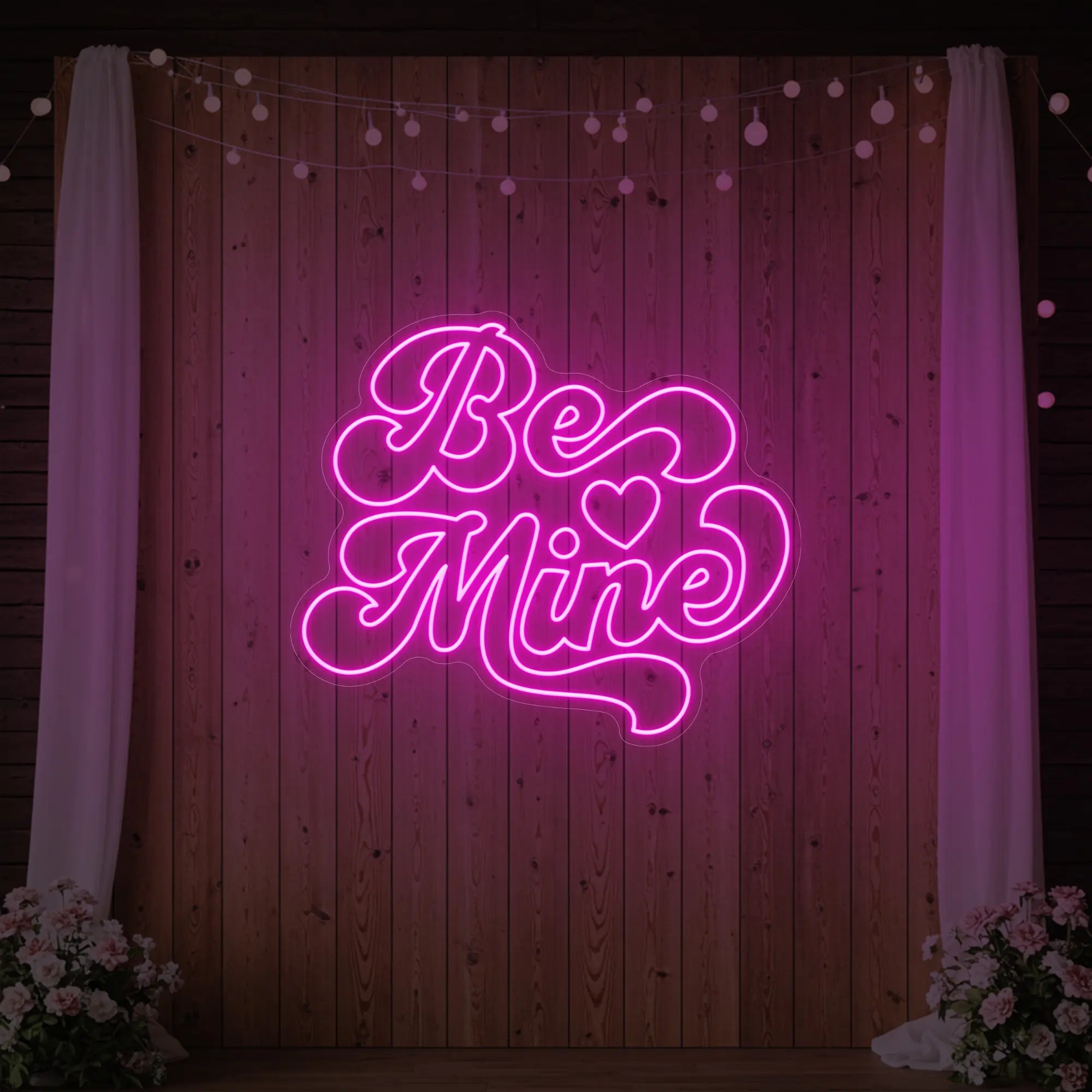 Photo of the 'Be Mine' neon sign glowing in light pink against a styled interior wall.