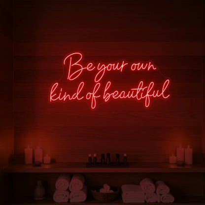 Photo of the 'Be Your Own Kind of Beautiful' neon sign glowing in red against a styled interior wall.