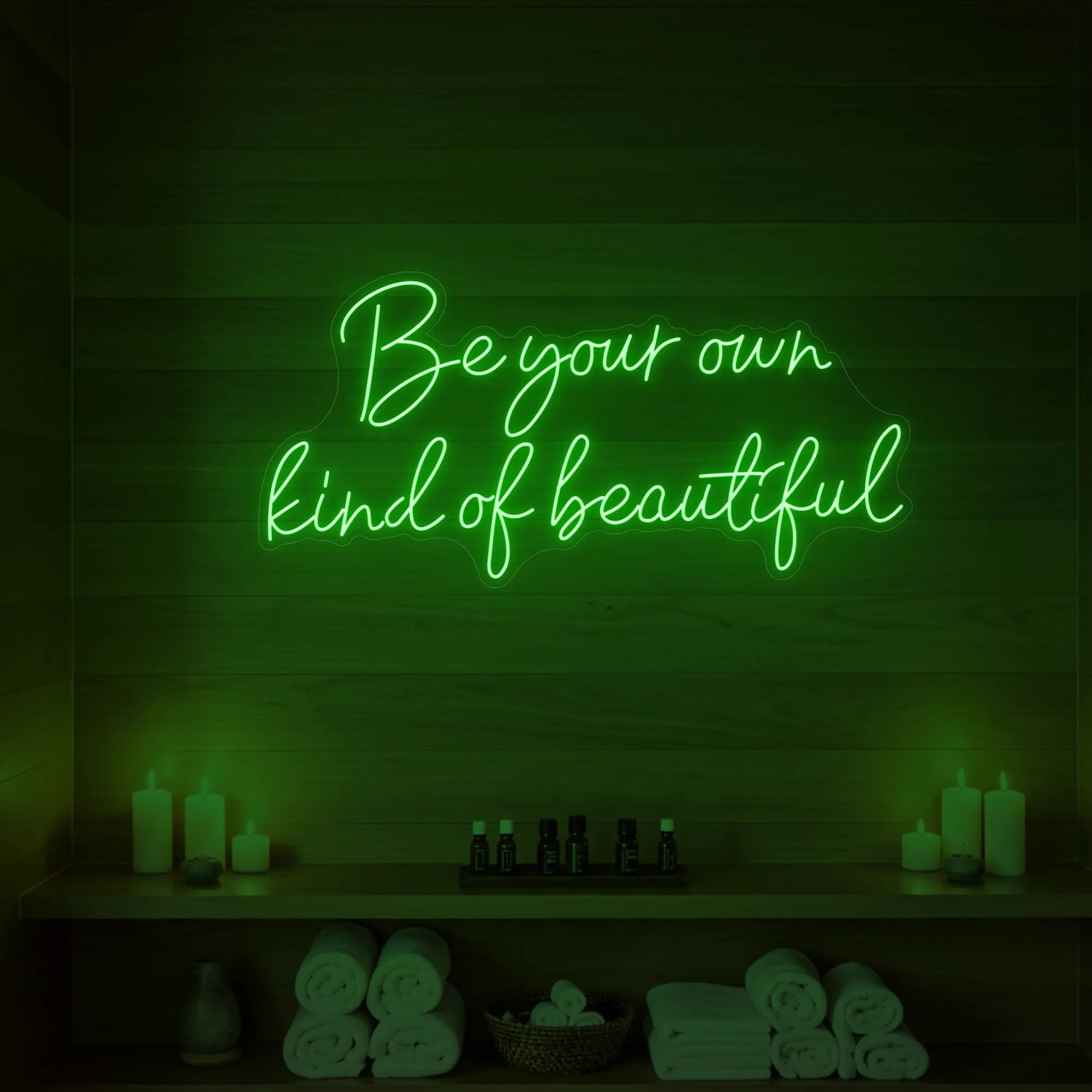 Photo of the 'Be Your Own Kind of Beautiful' neon sign glowing in green against a styled interior wall.