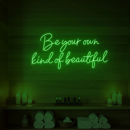 Photo of the 'Be Your Own Kind of Beautiful' neon sign glowing in green against a styled interior wall.
