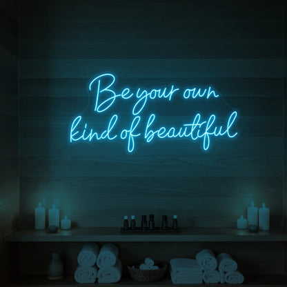 Photo of the 'Be Your Own Kind of Beautiful' neon sign glowing in ice blue against a styled interior wall.