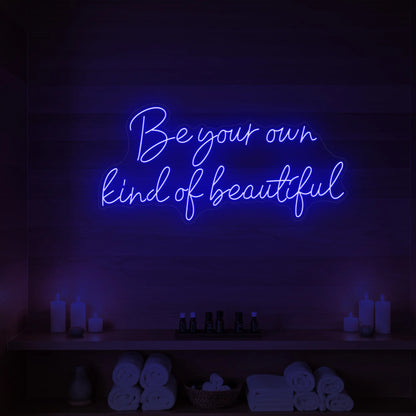 Photo of the 'Be Your Own Kind of Beautiful' neon sign glowing in deep blue against a styled interior wall.