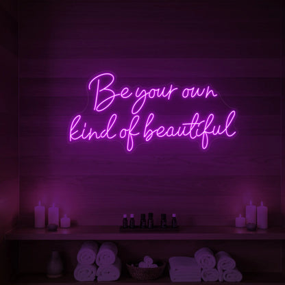 Photo of the 'Be Your Own Kind of Beautiful' neon sign glowing in deep pink against a styled interior wall.