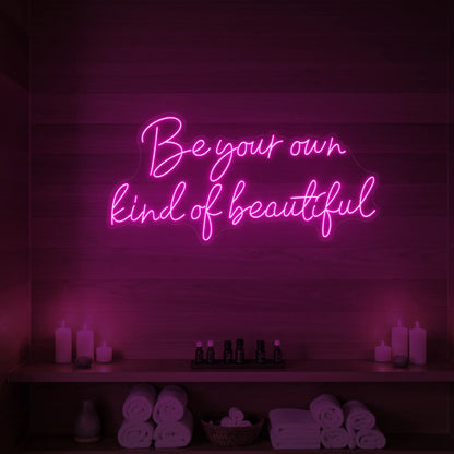 Photo of the 'Be Your Own Kind of Beautiful' neon sign glowing in light pink against a styled interior wall.