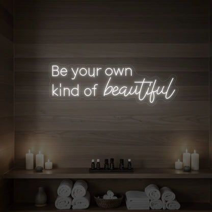 Photo of the 'Be your own kind of beautiful' neon sign glowing in cool white against a styled interior wall.