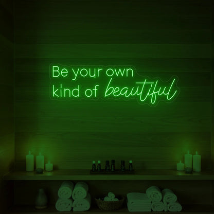 Photo of the 'Be your own kind of beautiful' neon sign glowing in green against a styled interior wall.
