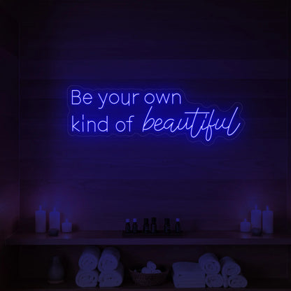 Photo of the 'Be your own kind of beautiful' neon sign glowing in deep blue against a styled interior wall.