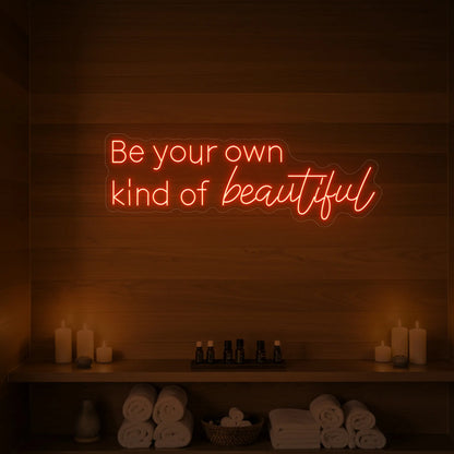 Photo of the 'Be your own kind of beautiful' neon sign glowing in golden yellow against a styled interior wall.