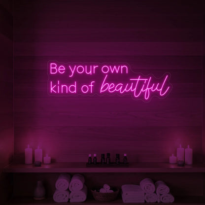 Photo of the 'Be your own kind of beautiful' neon sign glowing in light pink against a styled interior wall.