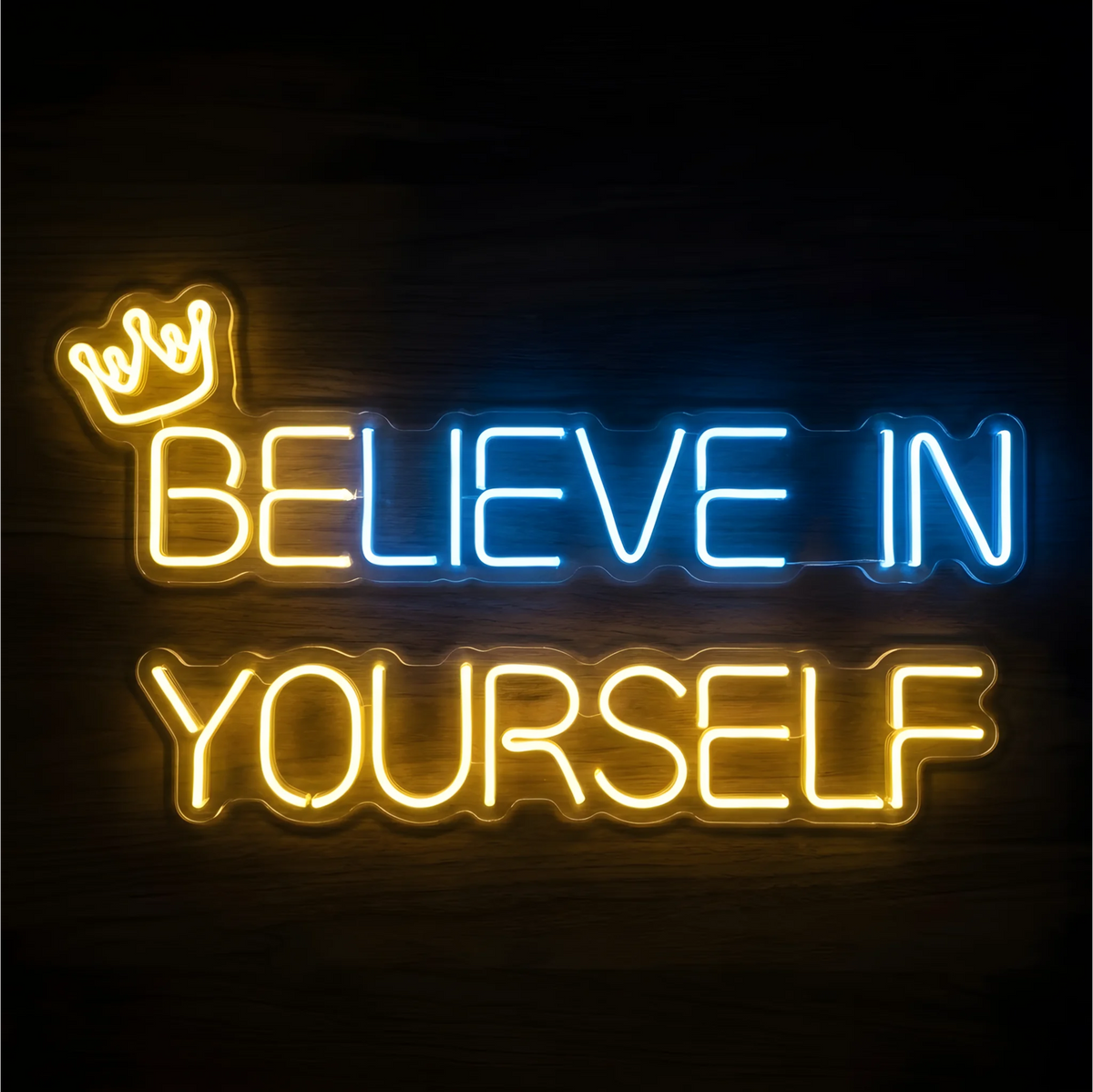 “BELIEVE IN YOURSELF” LED Neon Sign with blue “BELIEVE,” yellow “YOURSELF,” and a small yellow crown above the first word, displayed on clear acrylic against a dark wood background, suited to bedrooms and study spaces.