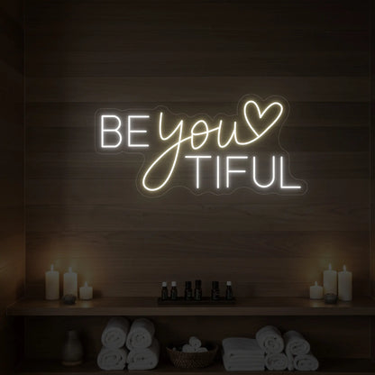 Photo of the 'BEYOUtiful' neon sign glowing in warm white against a styled interior wall.