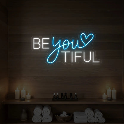 Photo of the 'BEYOUtiful' neon sign glowing in ice blue against a styled interior wall.