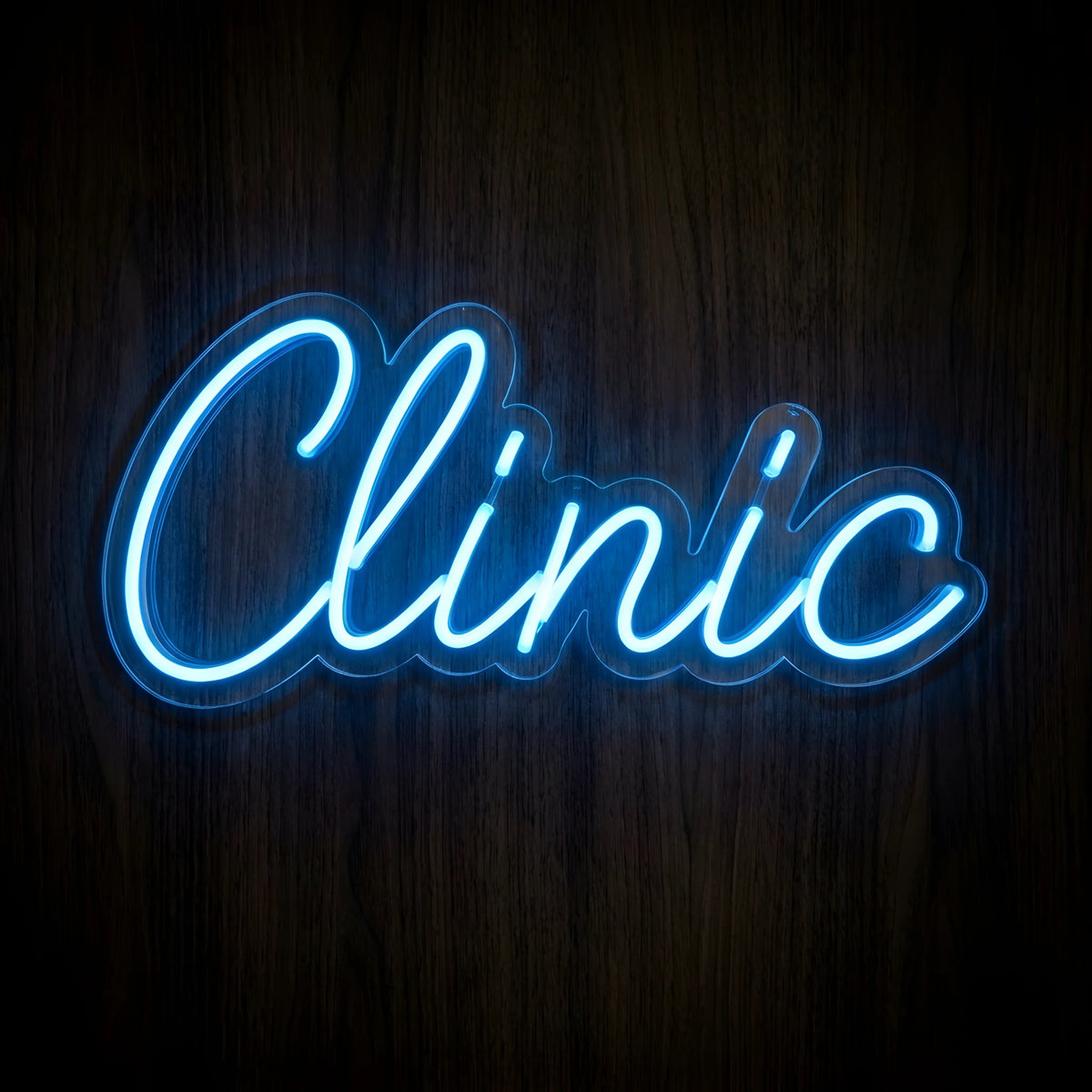 Blue Clinic Script LED Neon Sign featuring elegant cursive Clinic lettering in bright blue neon on clear cut-to-shape acrylic backing against a dark wooden wall.