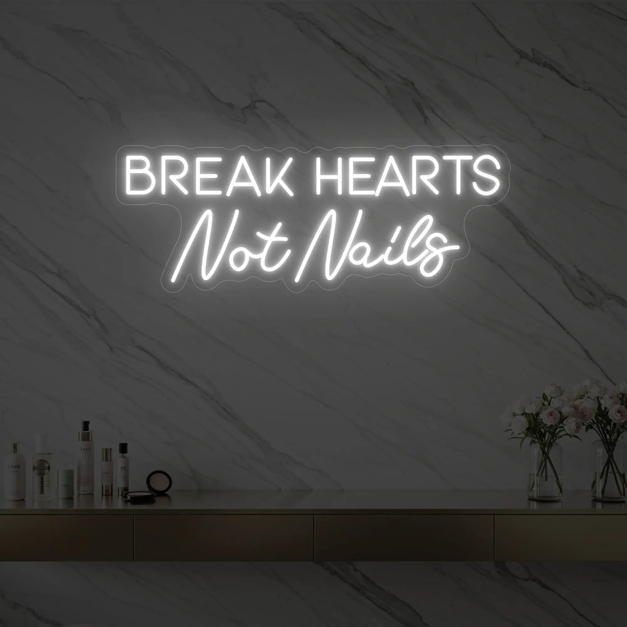 Photo of the 'BREAK HEARTS Not Nails' neon sign glowing in cool white against a styled interior wall.