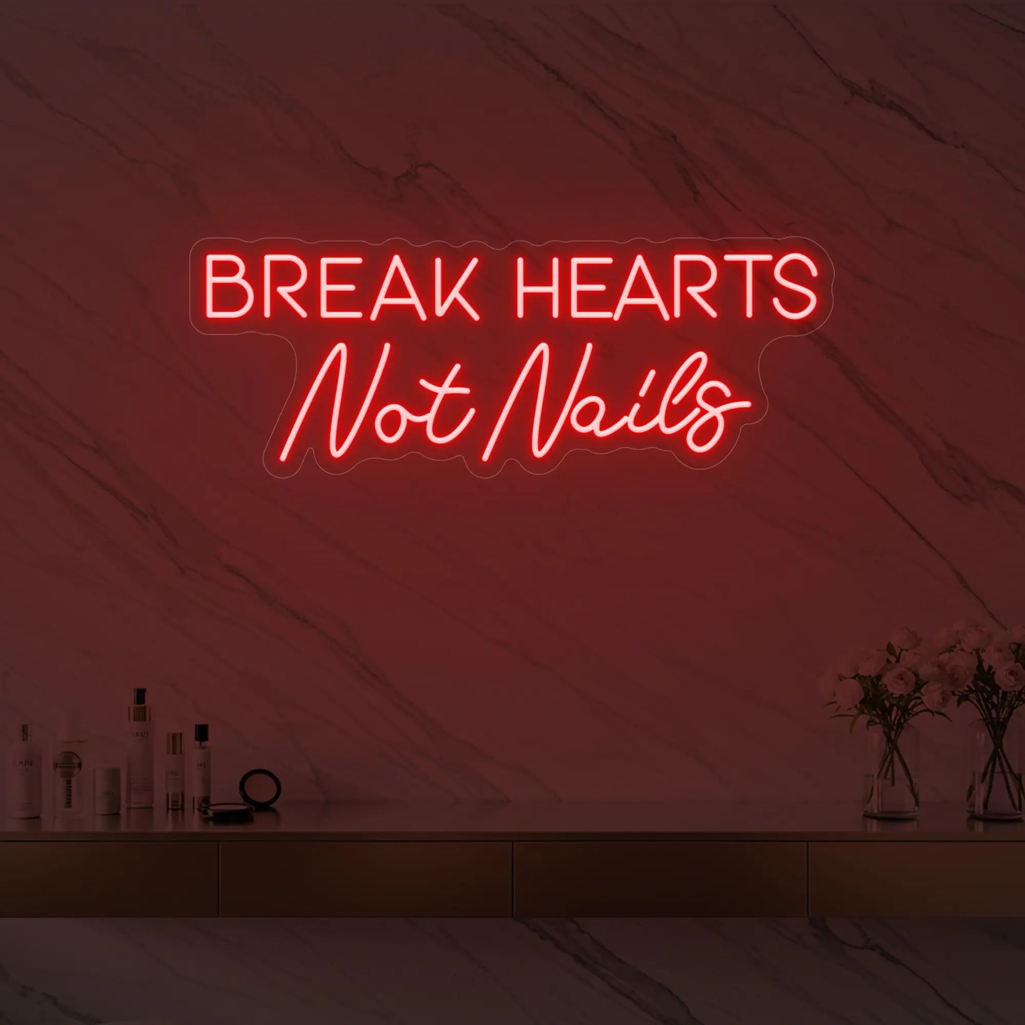 Photo of the 'BREAK HEARTS Not Nails' neon sign glowing in red against a styled interior wall.