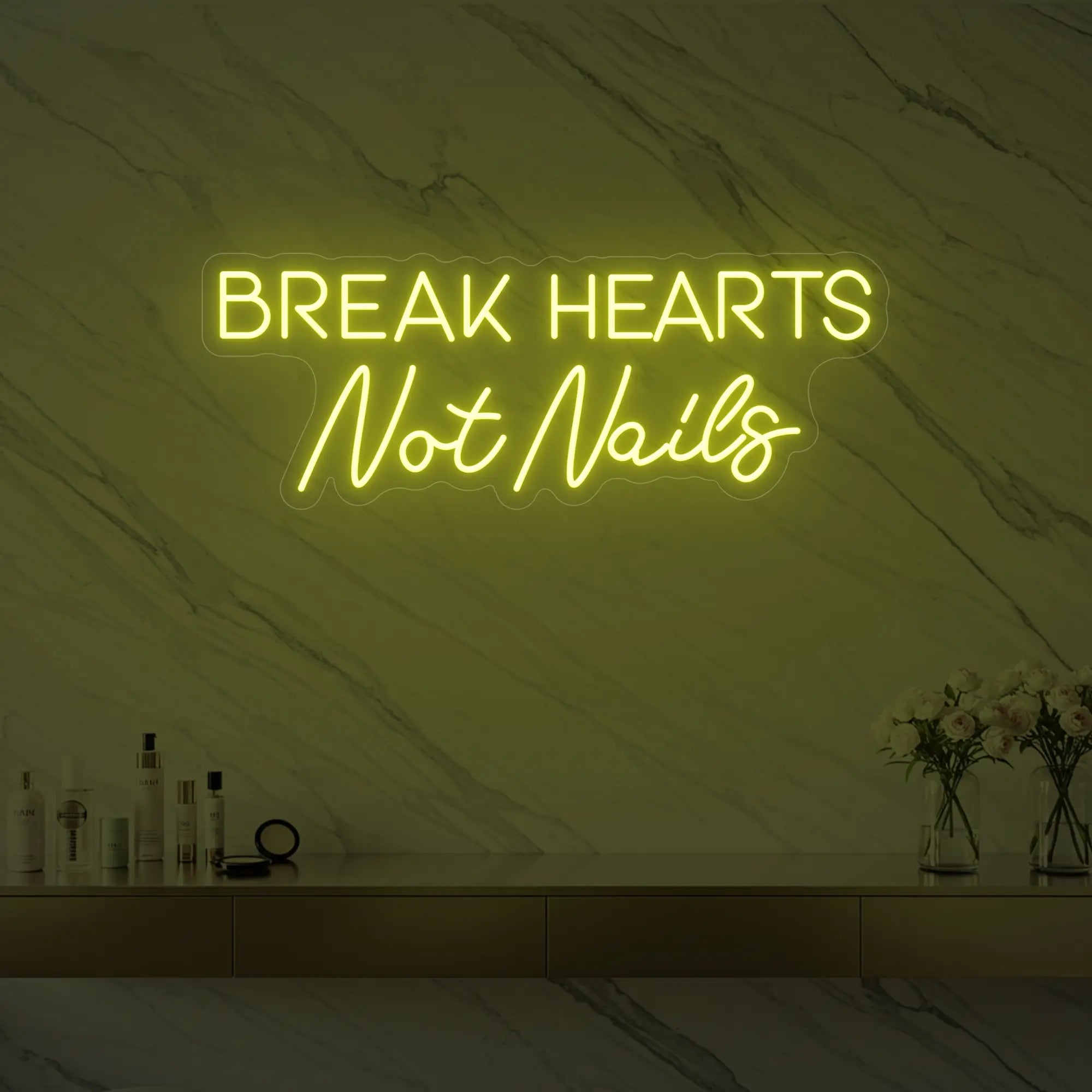 Photo of the 'BREAK HEARTS Not Nails' neon sign glowing in lemon yellow against a styled interior wall.