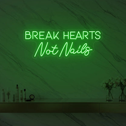 Photo of the 'BREAK HEARTS Not Nails' neon sign glowing in green against a styled interior wall.