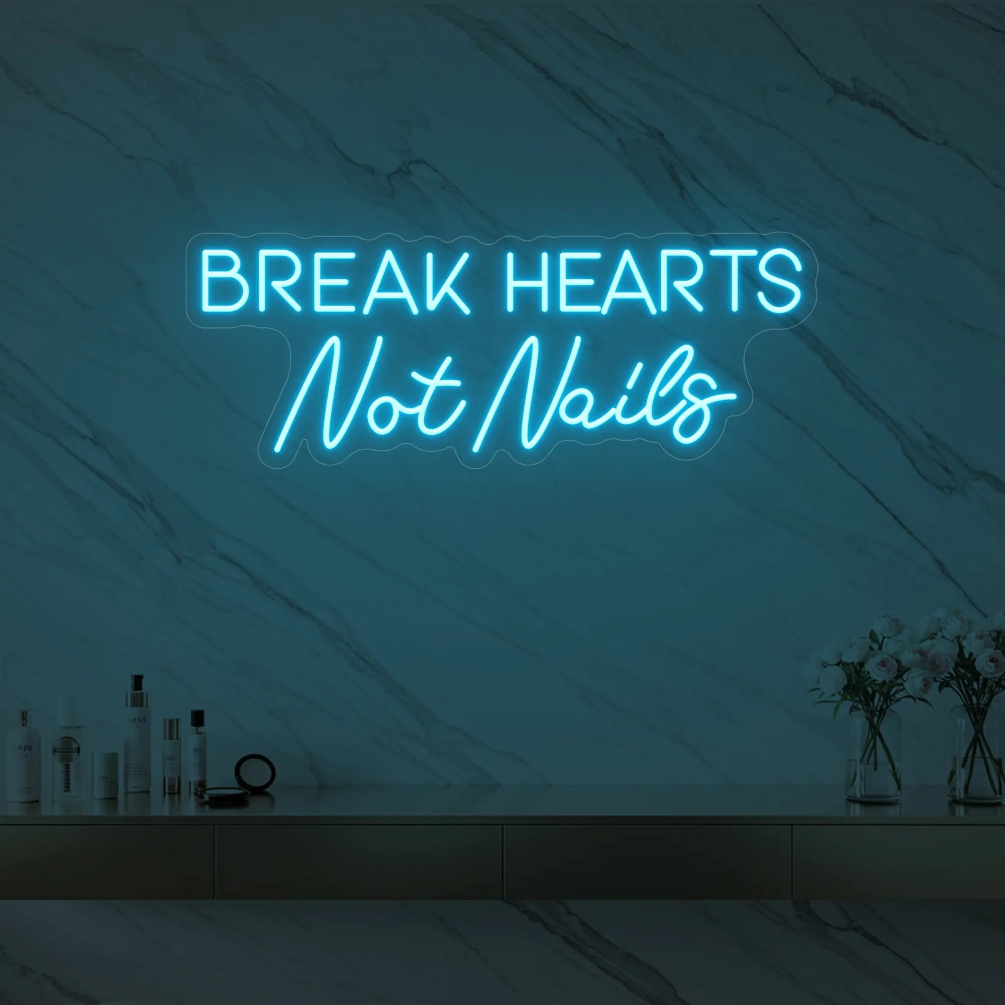 Photo of the 'BREAK HEARTS Not Nails' neon sign glowing in ice blue against a styled interior wall.