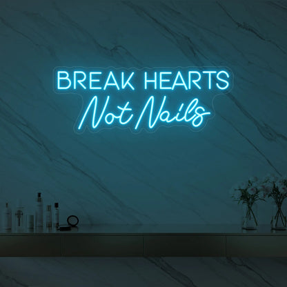 Photo of the 'BREAK HEARTS Not Nails' neon sign glowing in ice blue against a styled interior wall.