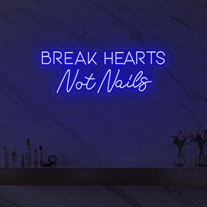 Photo of the 'BREAK HEARTS Not Nails' neon sign glowing in deep blue against a styled interior wall.