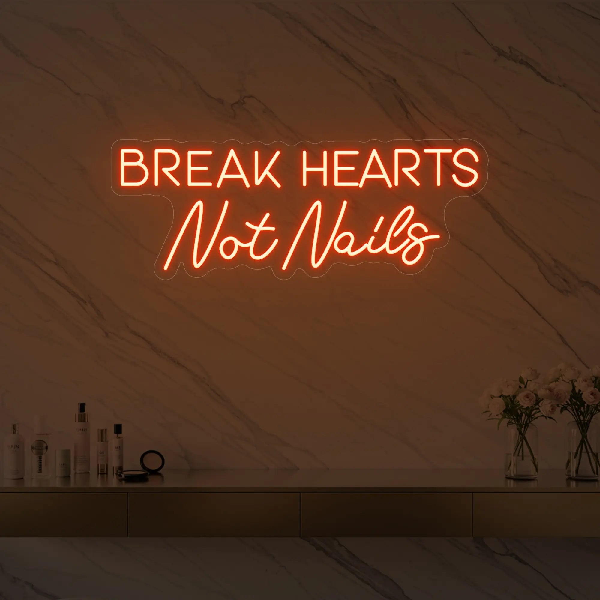Photo of the 'BREAK HEARTS Not Nails' neon sign glowing in golden yellow against a styled interior wall.