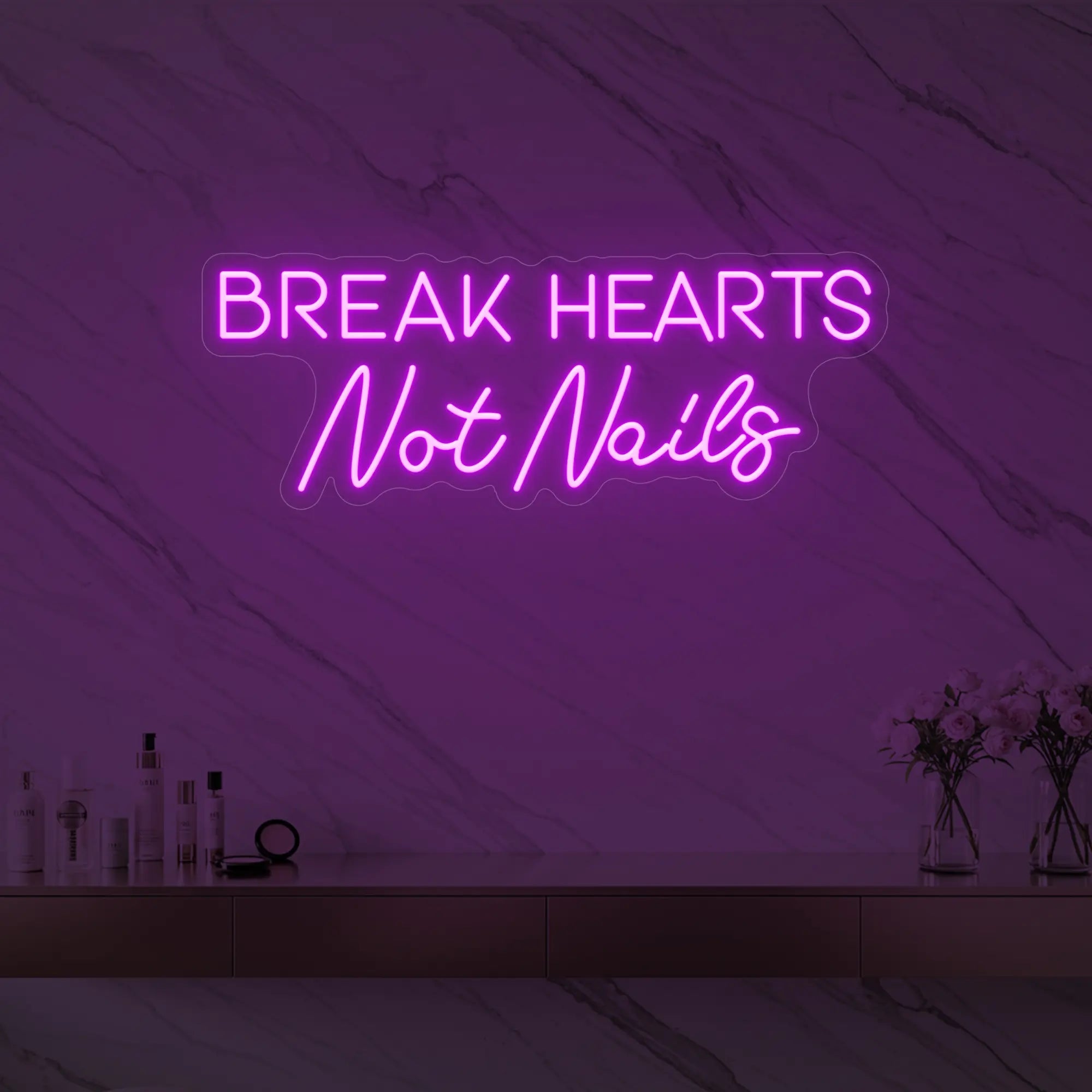 Photo of the 'BREAK HEARTS Not Nails' neon sign glowing in deep pink against a styled interior wall.