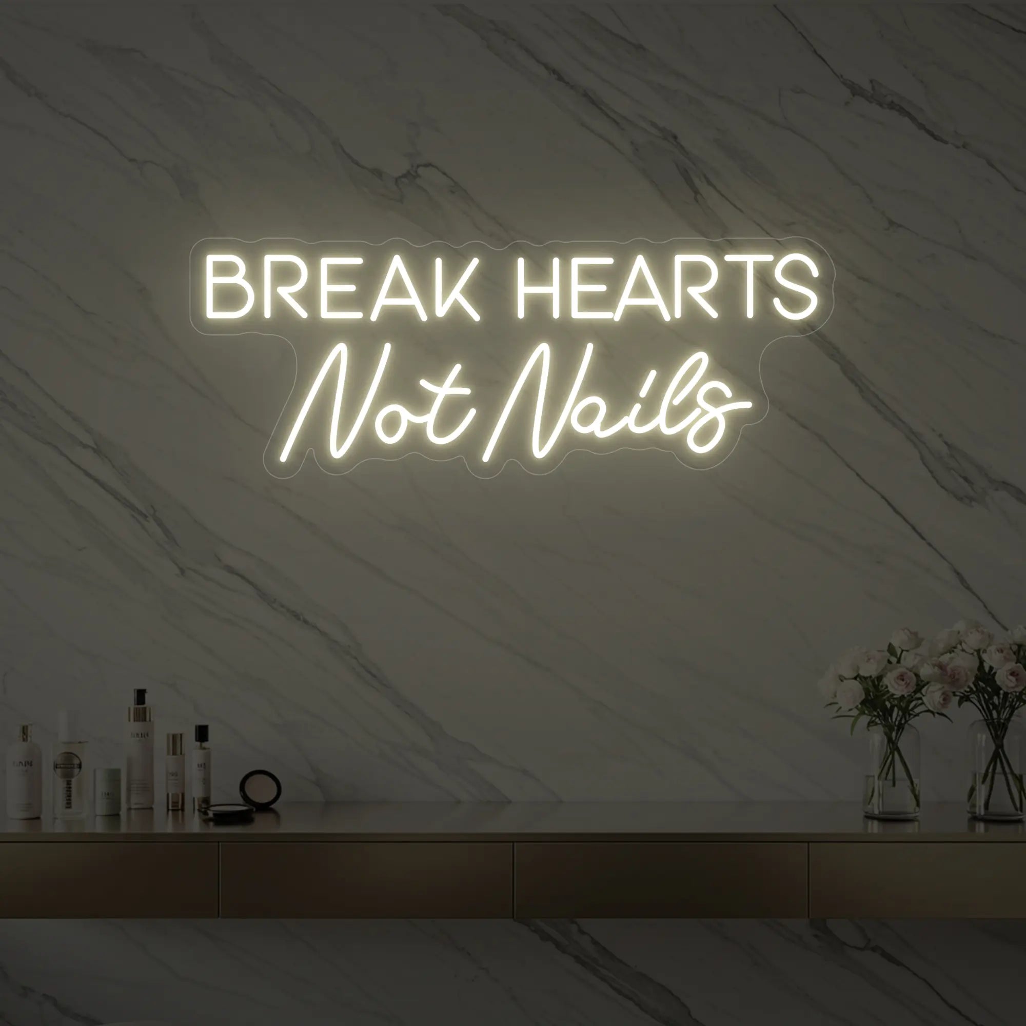 Photo of the 'BREAK HEARTS Not Nails' neon sign glowing in warm white against a styled interior wall.