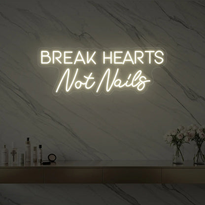 Photo of the 'BREAK HEARTS Not Nails' neon sign glowing in warm white against a styled interior wall.