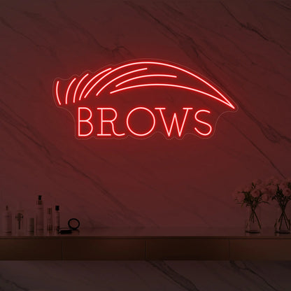 Photo of the 'BROWS' neon sign with an eyebrow graphic glowing in red against a styled interior wall.
