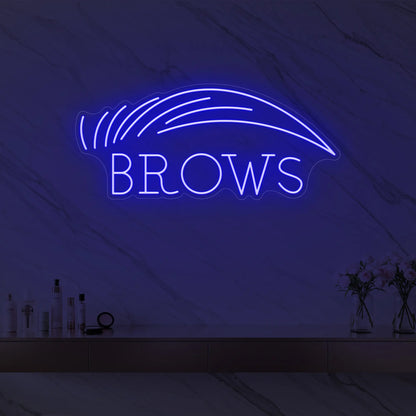 Photo of the 'BROWS' neon sign with an eyebrow graphic glowing in deep blue against a styled interior wall.