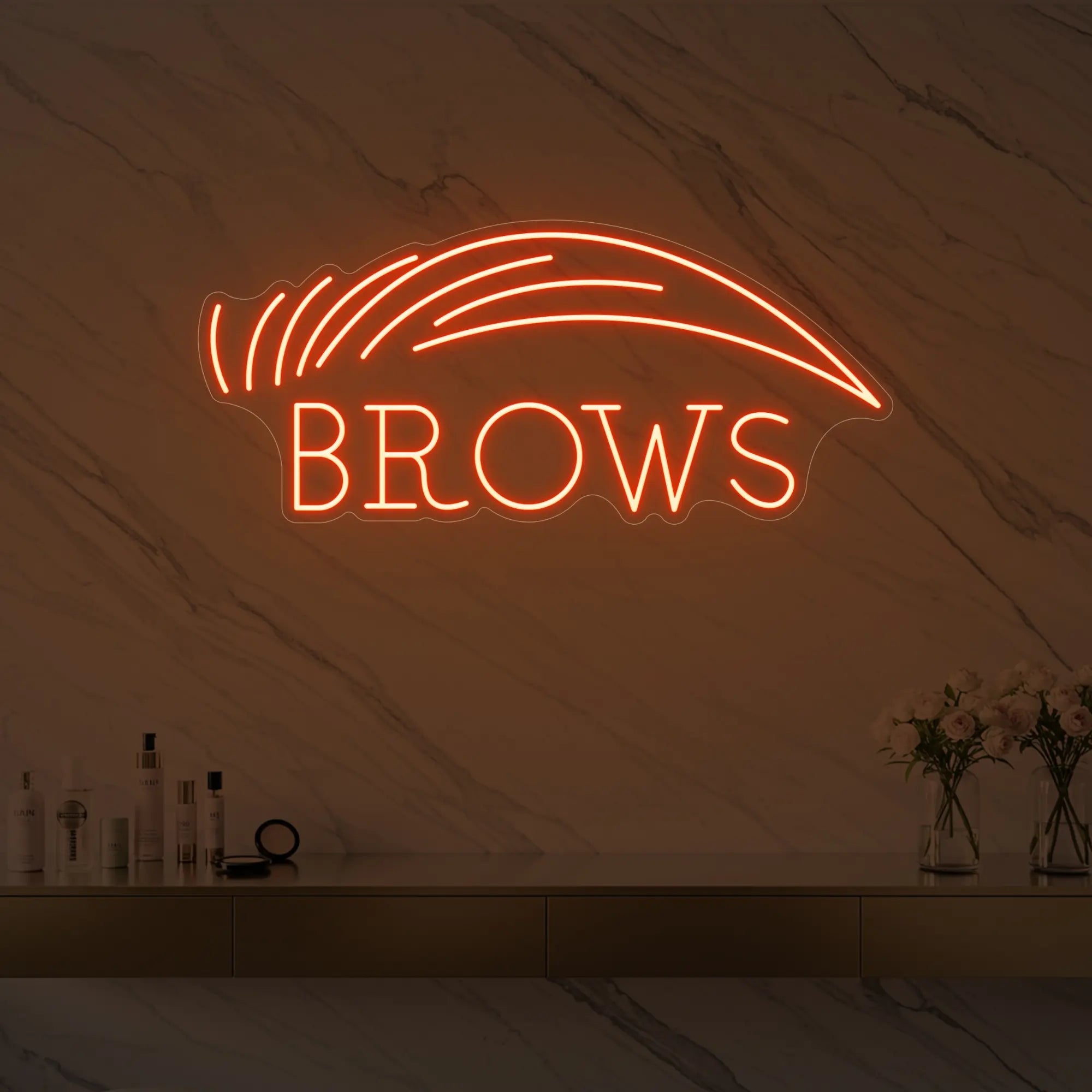 Photo of the 'BROWS' neon sign with an eyebrow graphic glowing in golden yellow against a styled interior wall.
