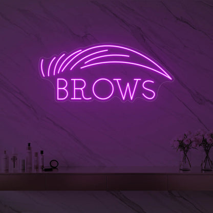 Photo of the 'BROWS' neon sign with an eyebrow graphic glowing in deep pink against a styled interior wall.