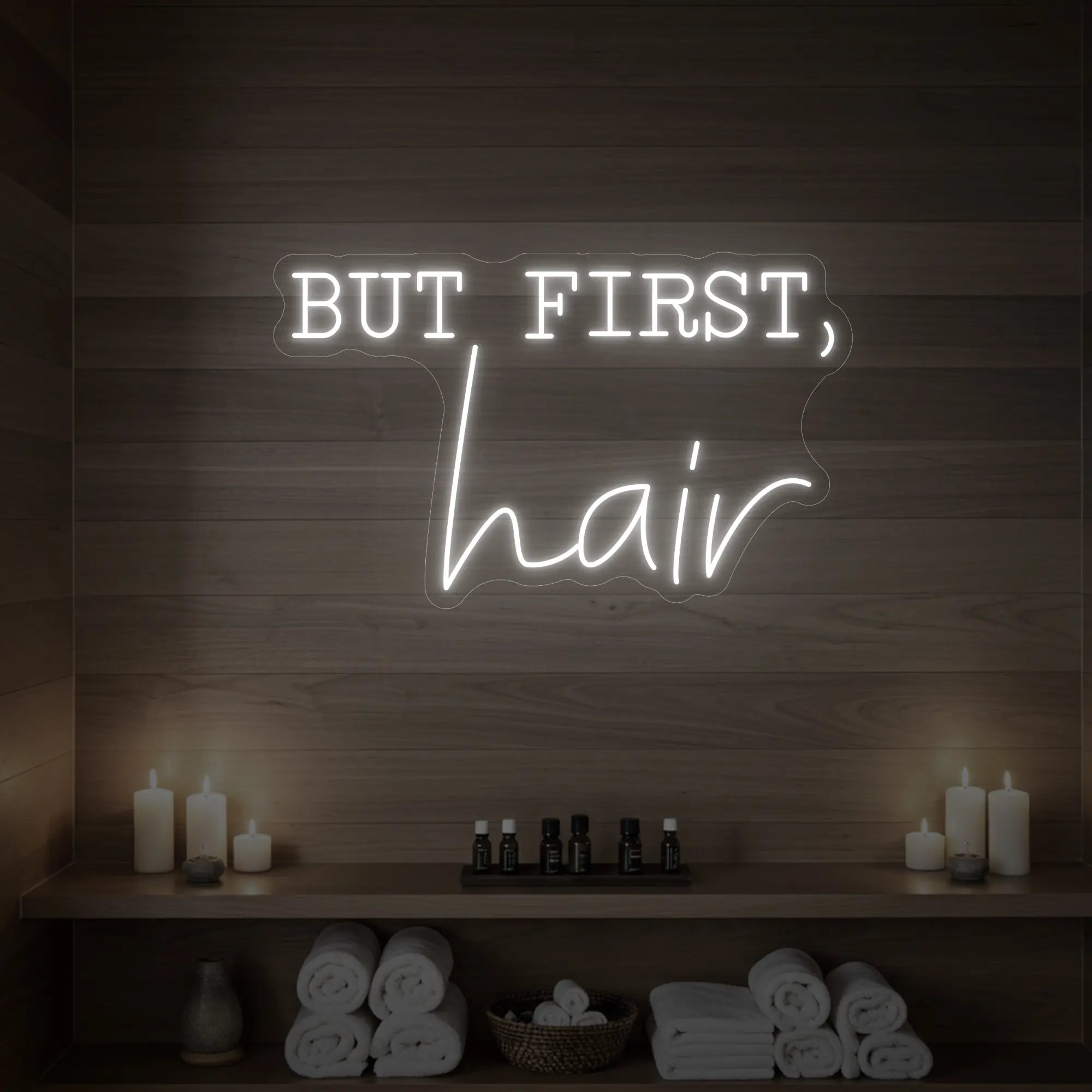 Photo of the 'BUT FIRST, hair' neon sign glowing in cool white against a styled interior wall.